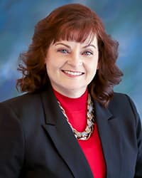 Professional woman with red hair wearing a black blazer and red top with a statement necklace