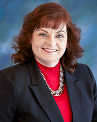 Professional woman with red hair wearing a black blazer and red top with a statement necklace