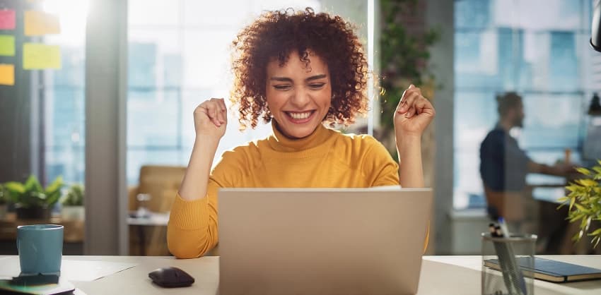 Excited woman celebrating good news on her laptop in a modern office