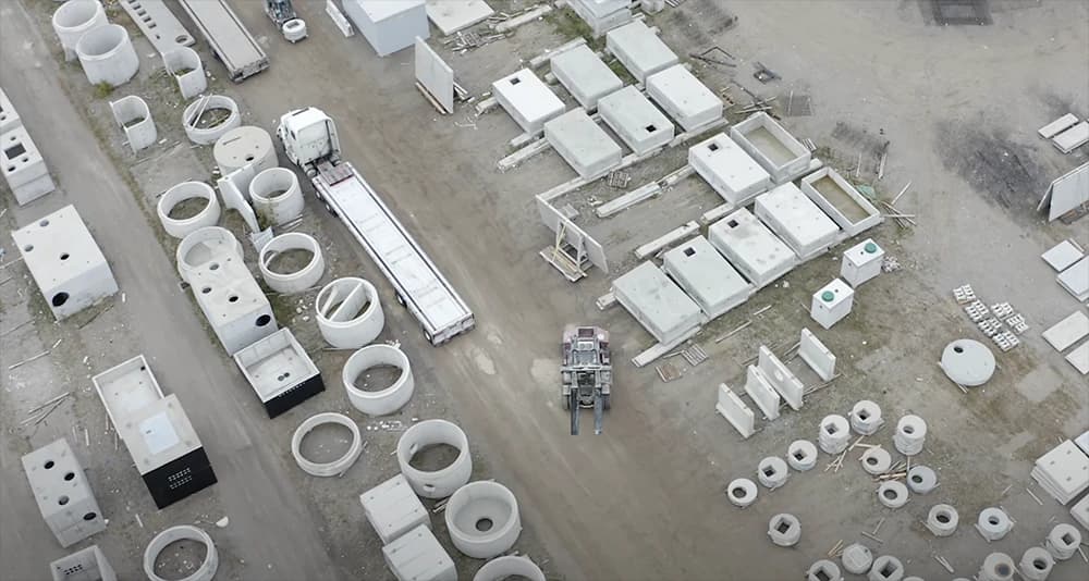 Aerial view of a precast concrete products yard with rings, boxes, and a forklift navigating the facility