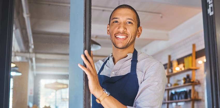 Cheerful small business owner in an apron welcoming customers at the door of their shop