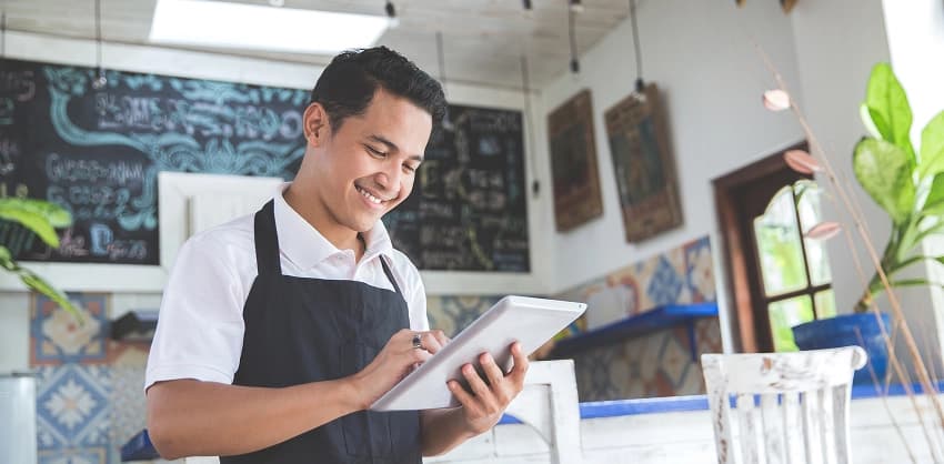 Smiling café worker in an apron using a tablet to manage business operations