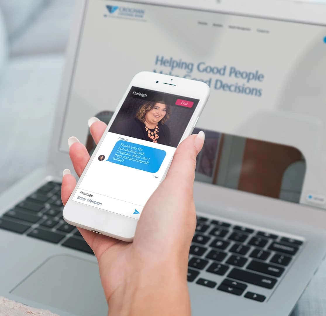 Person holding phone with Croghan Bank live chat open, laptop showing "Helping Good People Make Good Decisions" in background