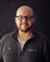 Croghan Bank wealth management professional smiling in a gray quarter-zip pullover against a dark background.