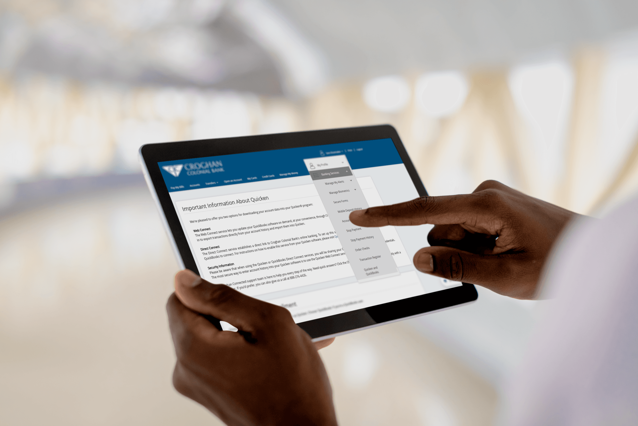 Hands holding a tablet displaying Croghan Colonial Bank's online banking interface with account management options.
